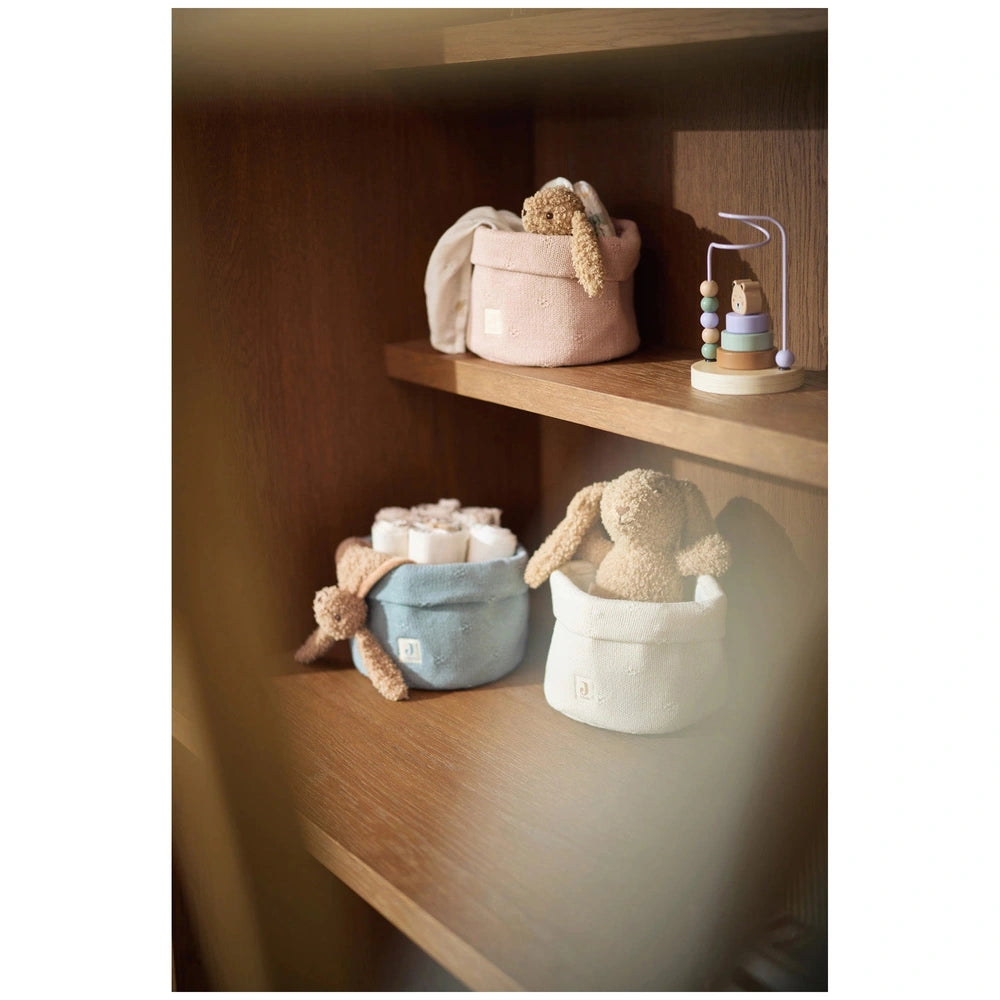 Jollein pacifier cloth bunny displayed on a shelf with pink, blue, and white teddy bears in matching baskets.