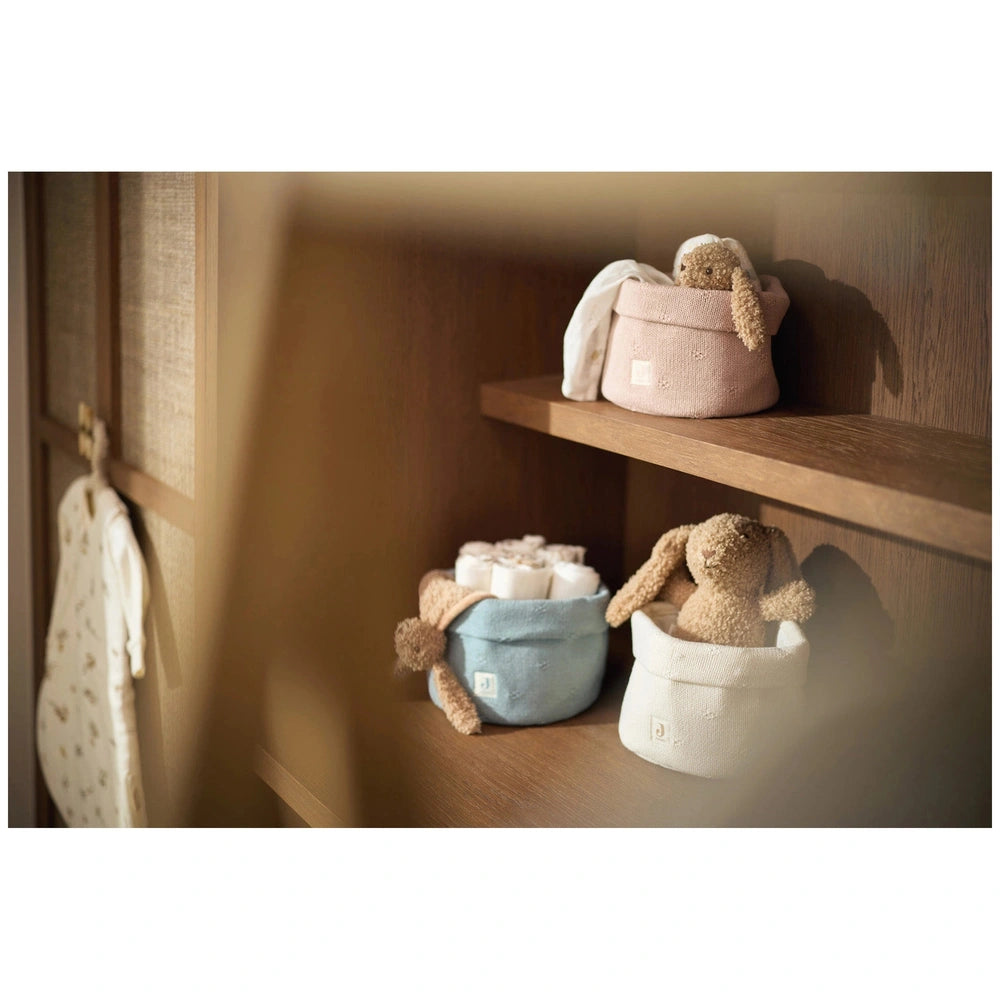 Jollein pacifier cloth bunny in beige on a wooden shelf alongside a brown stuffed animal and three colorful baskets.
