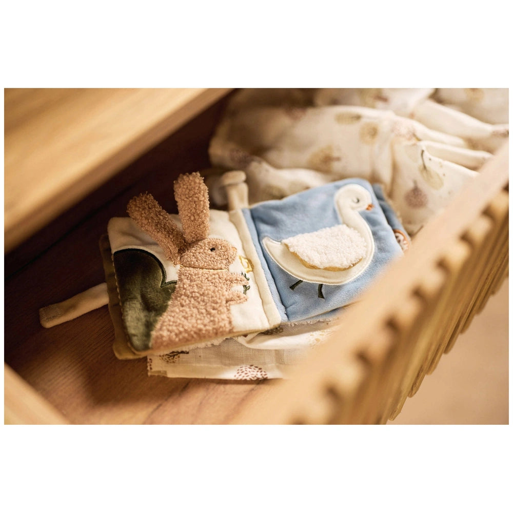 Jollein soft activity book features pink and white fabric, a blue duck, and a brown bunny on a wooden surface.