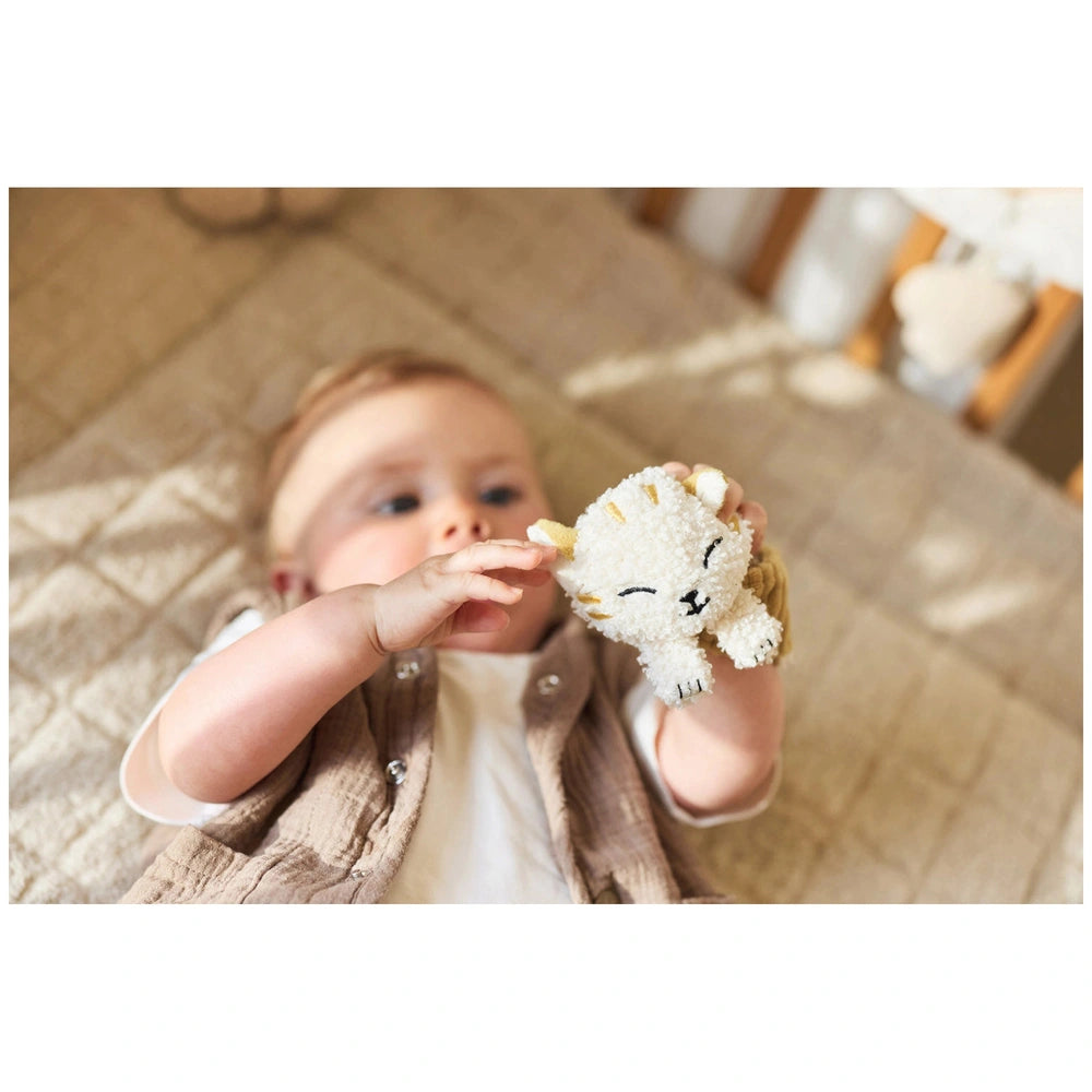 Jollein Wrist Rattle Tiny Park Charlie Cat, a baby holds a soft stuffed animal while wearing a white top and brown vest.