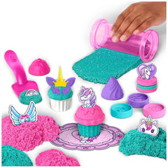 Kinetic Sand Unicorn Bake Shoppe features a hand holding a pink cupcake with unicorn decoration amidst colorful crafting item