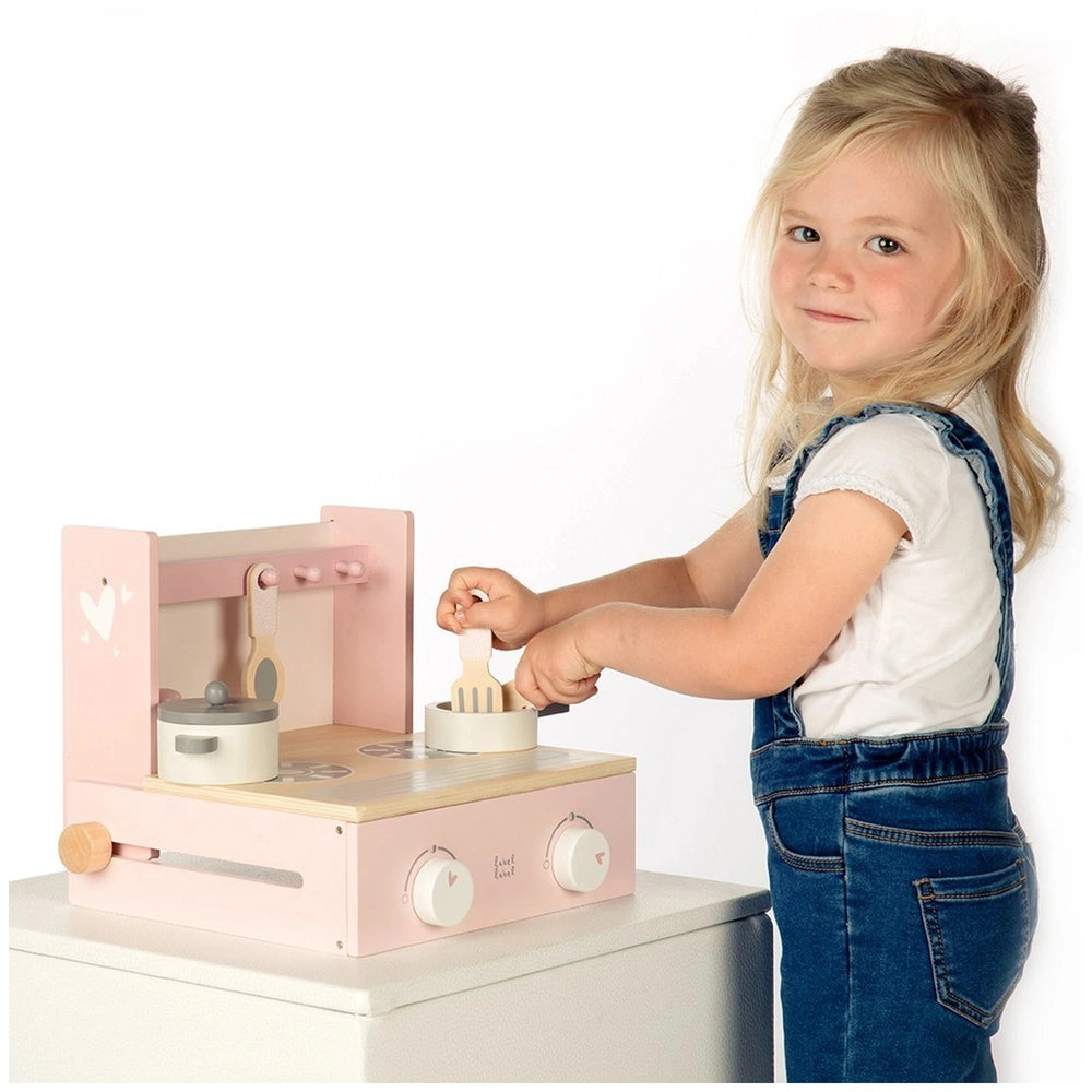 Foldable cooker toy kitchen with pink and white features, held by a young girl in blue overalls and a white shirt.