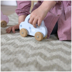 Blue plastic push and pull toy car with white roof, held by a child's hand wearing a pink top on textured fabric.
