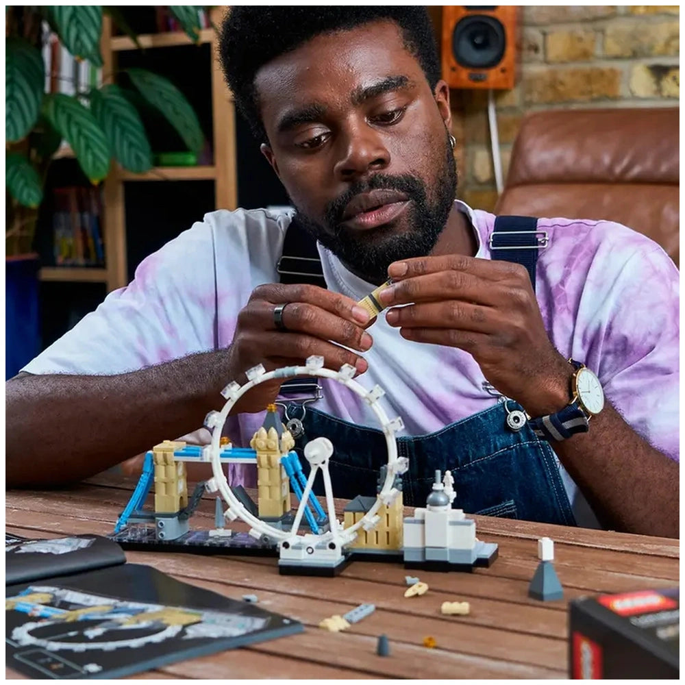 Lego Architecture London construction set is being assembled by a man at a wooden table with scattered train set components.