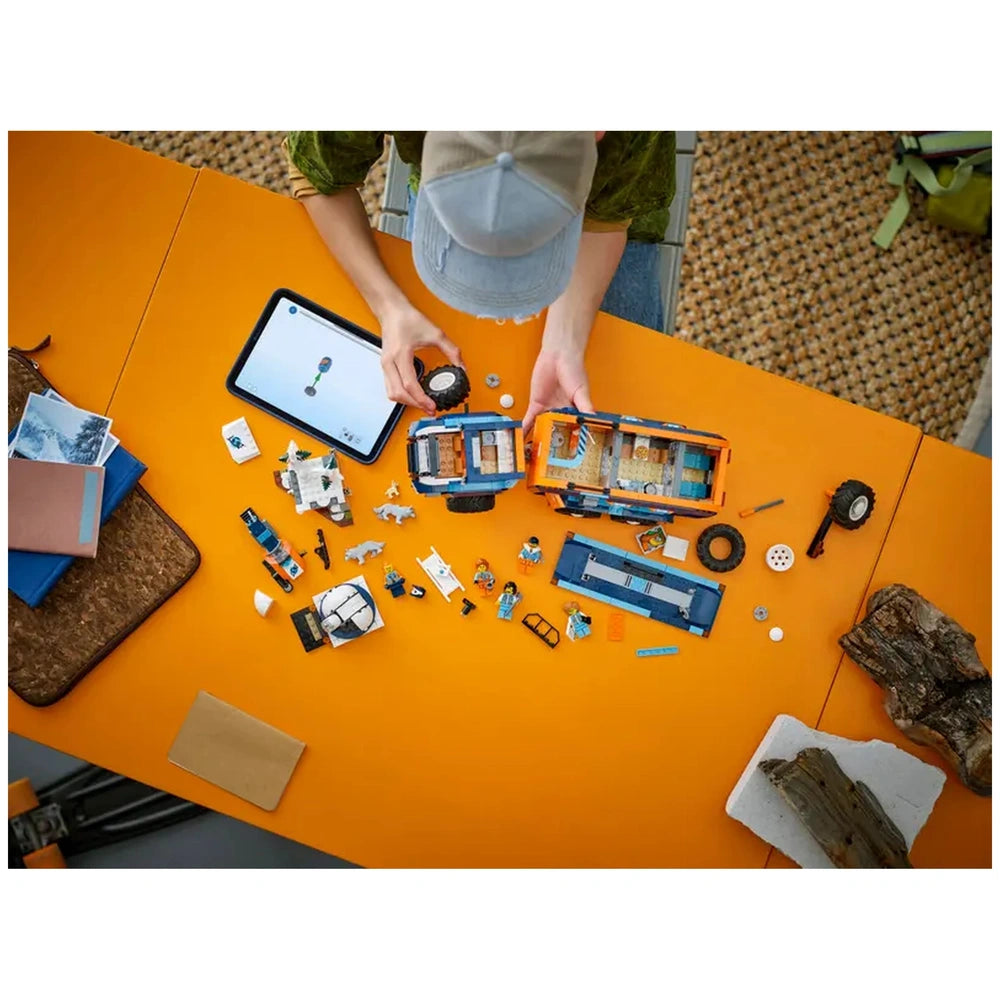 LEGO Arctic Explorer Science Lab Truck set displayed on an orange table with a person examining a toy car and laptop nearby.