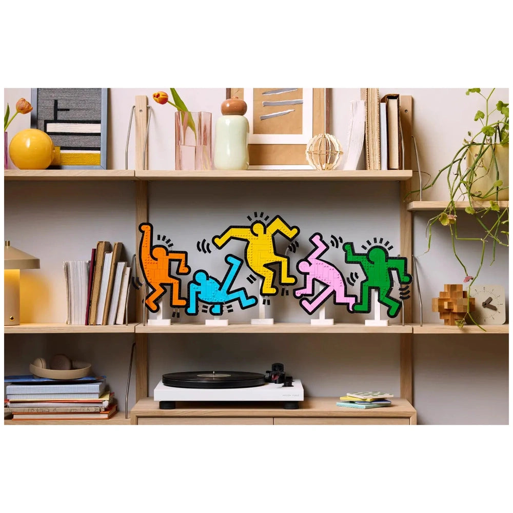 LEGO Art Keith Haring Dancing Figures displayed on a modern shelf alongside books, a clock, and a vase with a plant.
