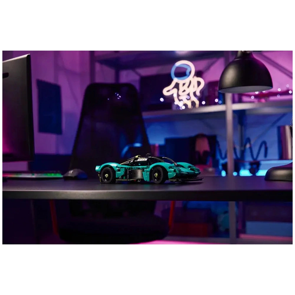LEGO Aston Martin Valkyrie construction set displayed on a dark desk in a purple-themed indoor setting.