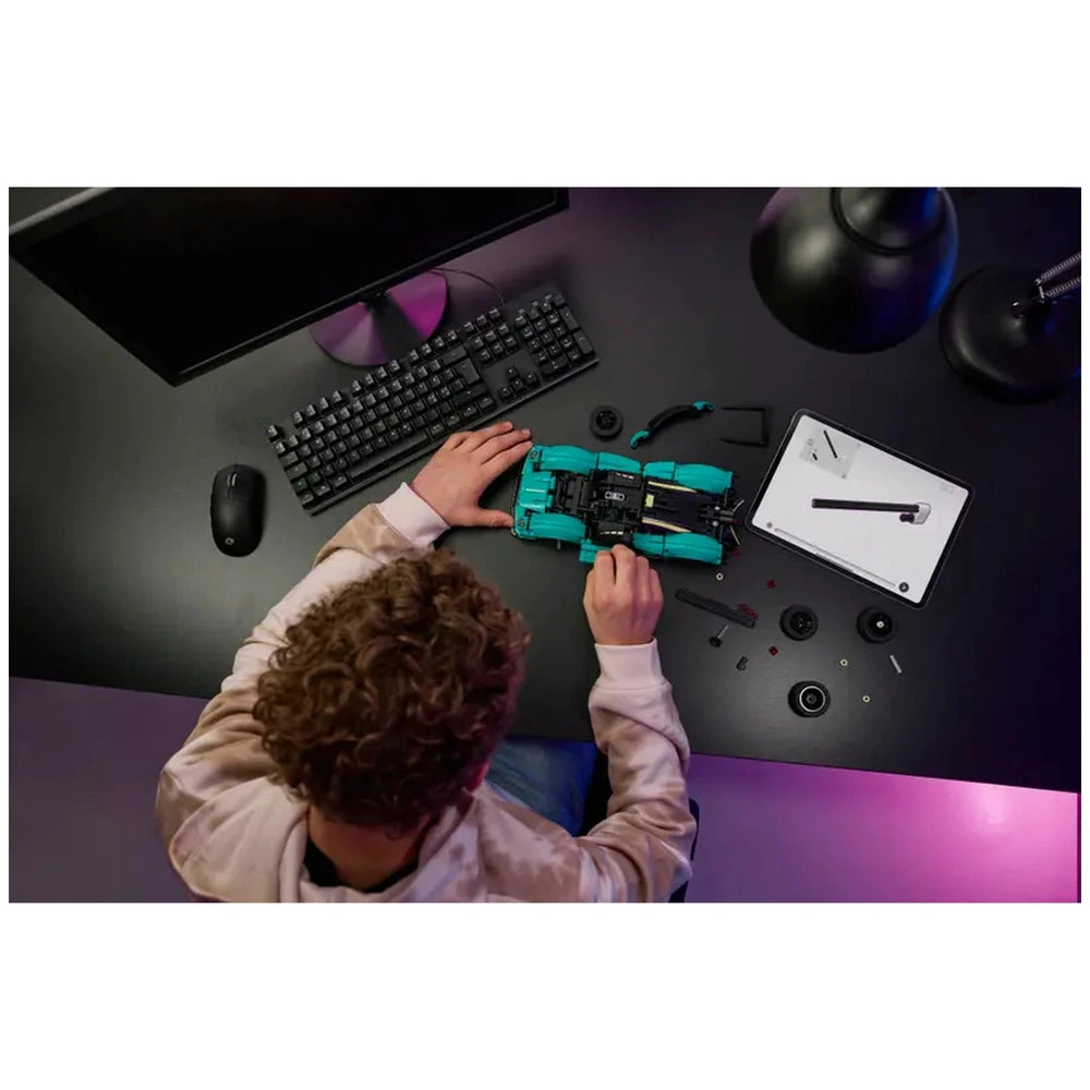 LEGO Aston Martin Valkyrie construction set displayed on a dark desk with scattered electronic parts and a person working.