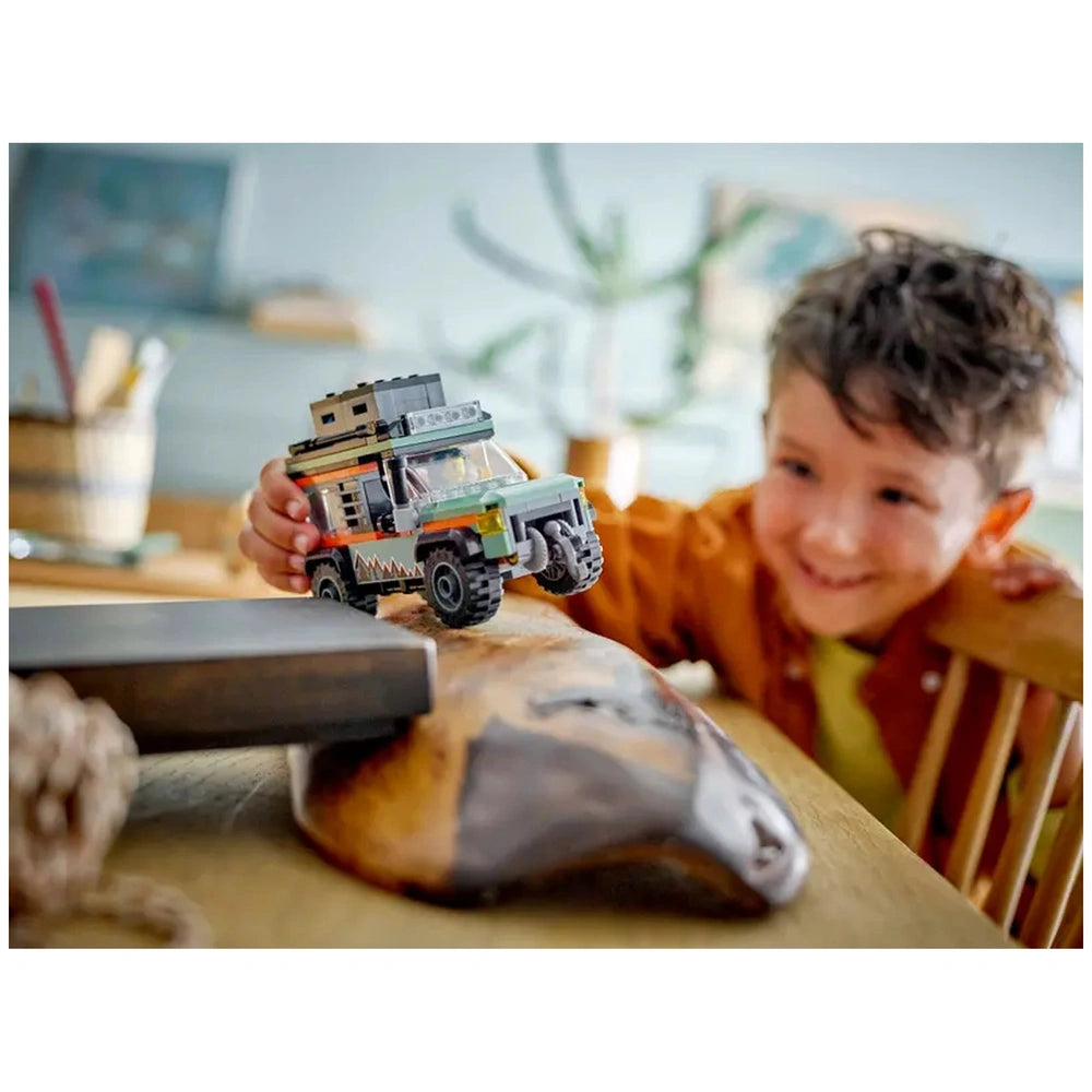 A child joyfully plays with the LEGO® City Off-Road Mountain Truck on a wooden table, showcasing vibrant colors and rugged details.