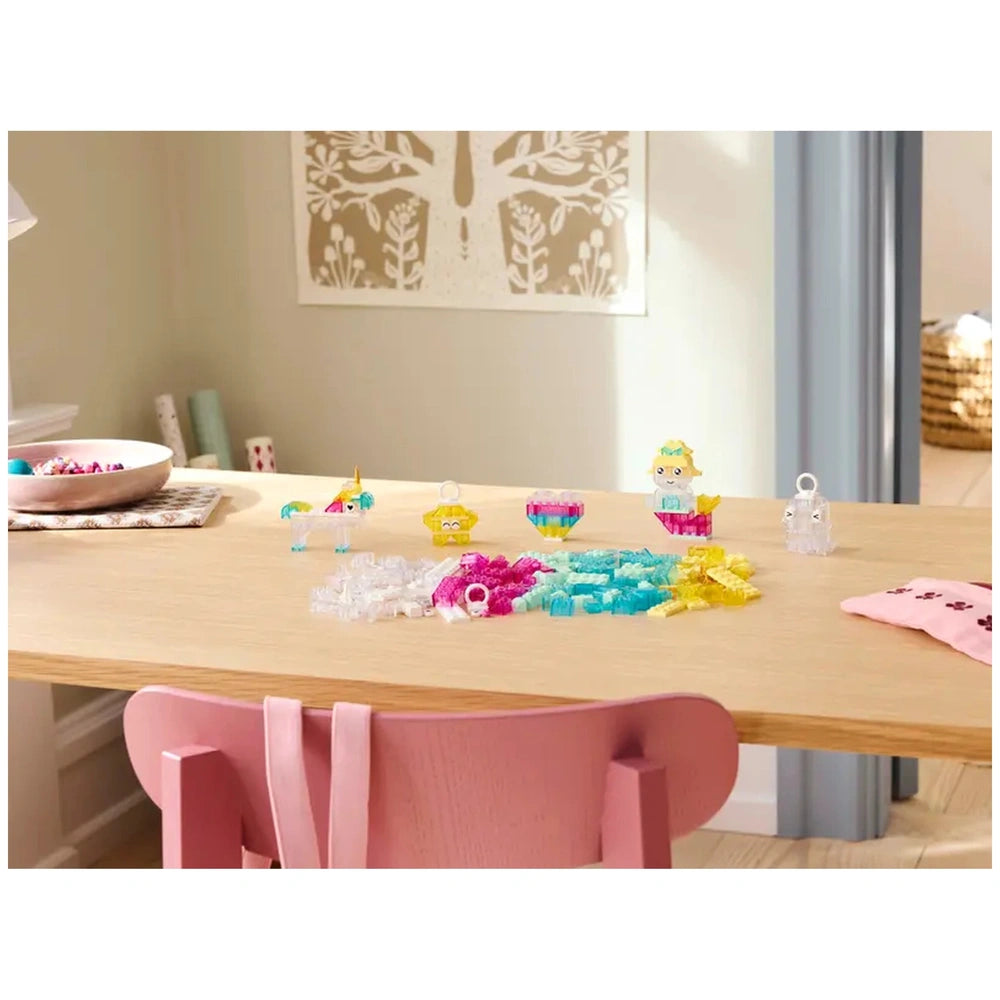 Colorful LEGO® pieces arranged on a wooden table, including transparent stars, a unicorn, and various whimsical creations, with a pink chair in view.
