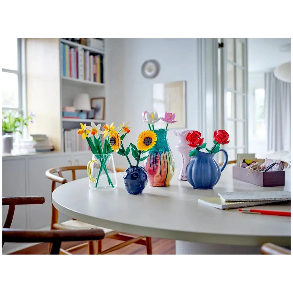 Colorful LEGO flowers arranged in various vases on a round white table, set in a bright, modern room with light wood accents.
