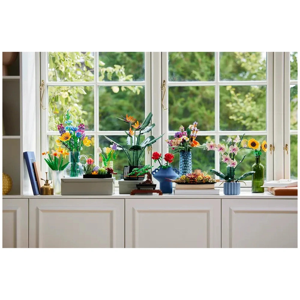 Colorful LEGO flower arrangements displayed on a windowsill, featuring sunflowers, orchids, and other blooms in various vases, brightening the space.