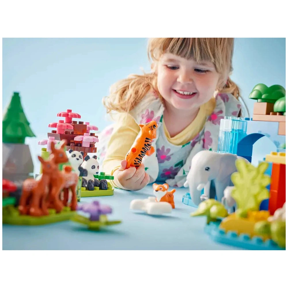 A smiling young girl holds an orange tiger figure, surrounded by colorful LEGO® DUPLO® animal toys, including an elephant and a panda, set against a blue backdrop.