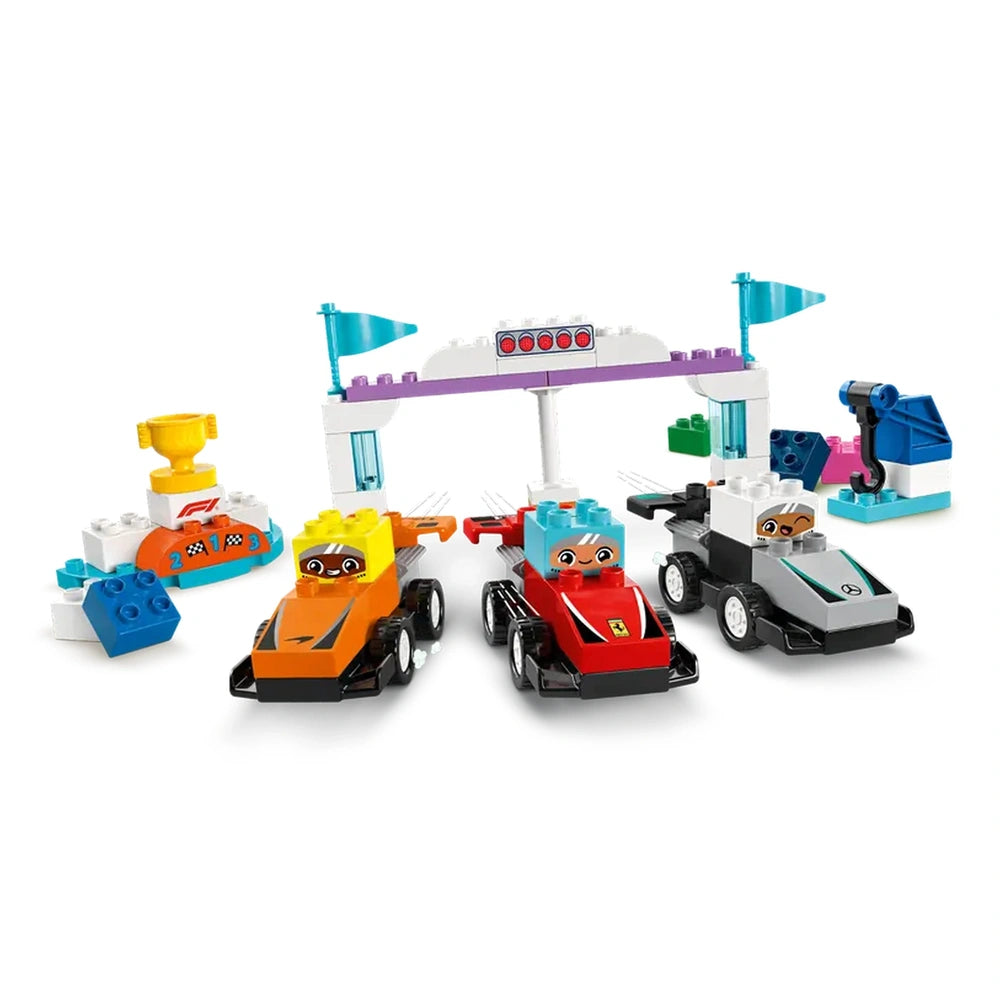 Three colorful race cars, orange, red, and black, are positioned at a starting line with a colorful arch and race flags. A winner's trophy and other racing elements create an exciting Formula 1® atmosphere.