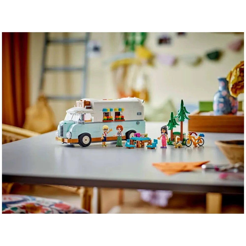 LEGO Friends Friendship Camper Van Adventure set featuring a light blue camper van, three minidolls, a picnic table, trees, and a bicycle on a table.