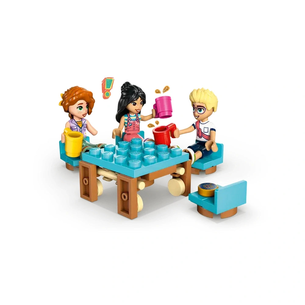 Three LEGO Friends minidolls at a colorful table, playfully sharing drinks in vibrant cups, with playful accessories around them.