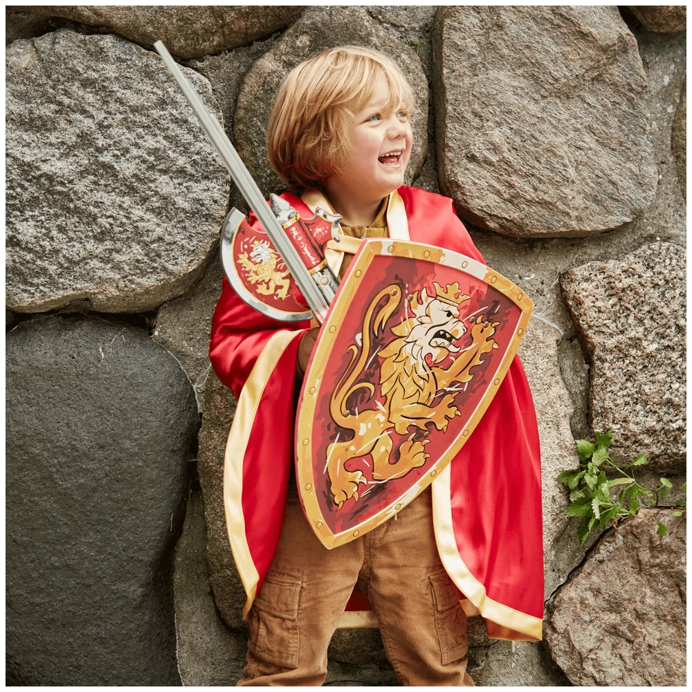 Young child in a shiny red costume with a yellow lion emblem, holding a red and yellow Knight sword against a rock wall.