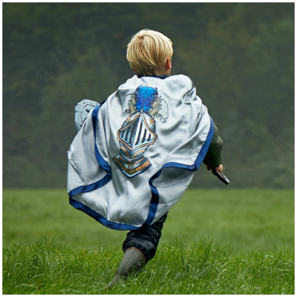 Liontouch Mystery Knight Cape worn by a child in a shiny white and blue jacket, standing on grass while holding a small objec