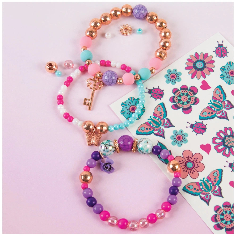 Bedazzled charm bracelet featuring gold and colorful beads on a metallic chain, displayed on floral patterned matte paper.