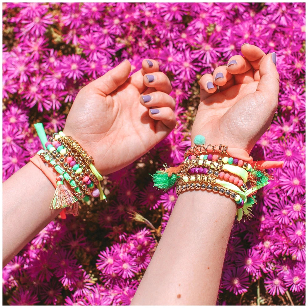 Neo-Brite Chains and Charms bracelets with colorful beads and tassels resting on artificial pink flowers and light purple nai