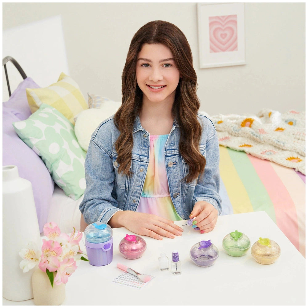 MAKE IT REAL Party Nails Glitter Nail Studio with various white nail polish bottles on a white table amidst a colorful bedroo