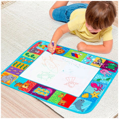 Molto Big Doodle Playmat with a child in a yellow shirt drawing with a crayon on a colorful mat on a white carpeted floor.