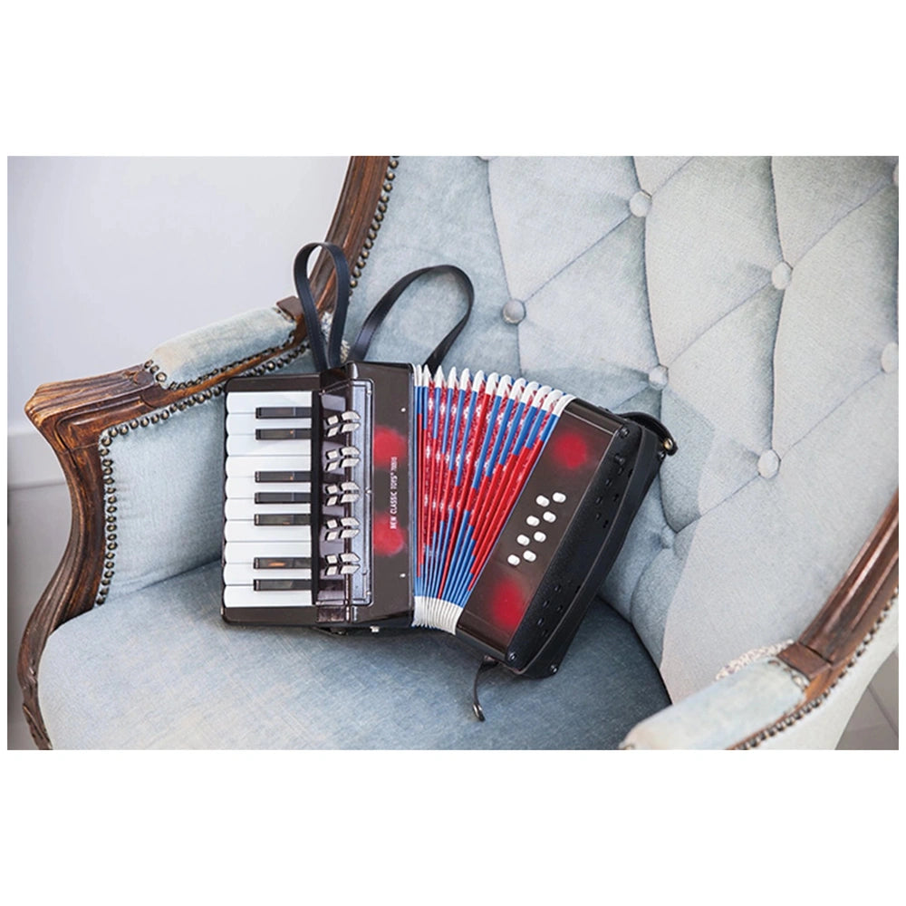Black accordion with red and blue keys and bellows design rests on a light blue patterned chair, accompanied by a music book.