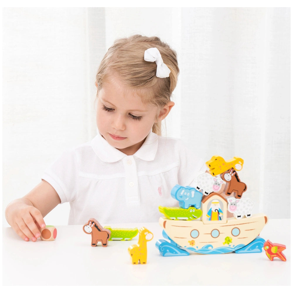 Balance Game Noah's Ark features a young girl in a white shirt playing with colorful plastic toy animals and a wooden-texture