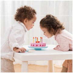 New Classic Toys Cutting Cake set with pink cake, blue candle holder, and two children celebrating at a white table.