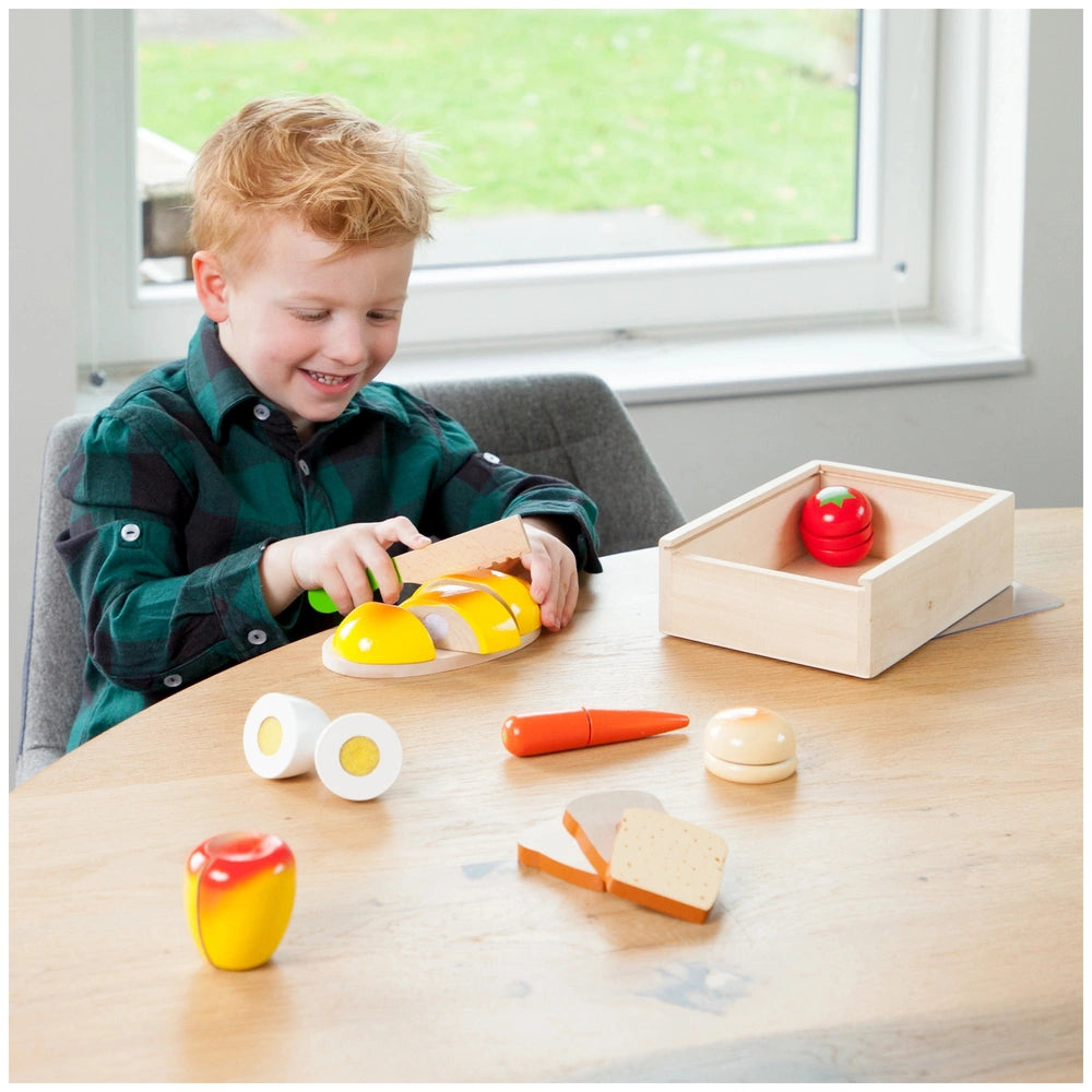 New Classic Toys breakfast box features a young child playing with plastic food items on a wooden table.