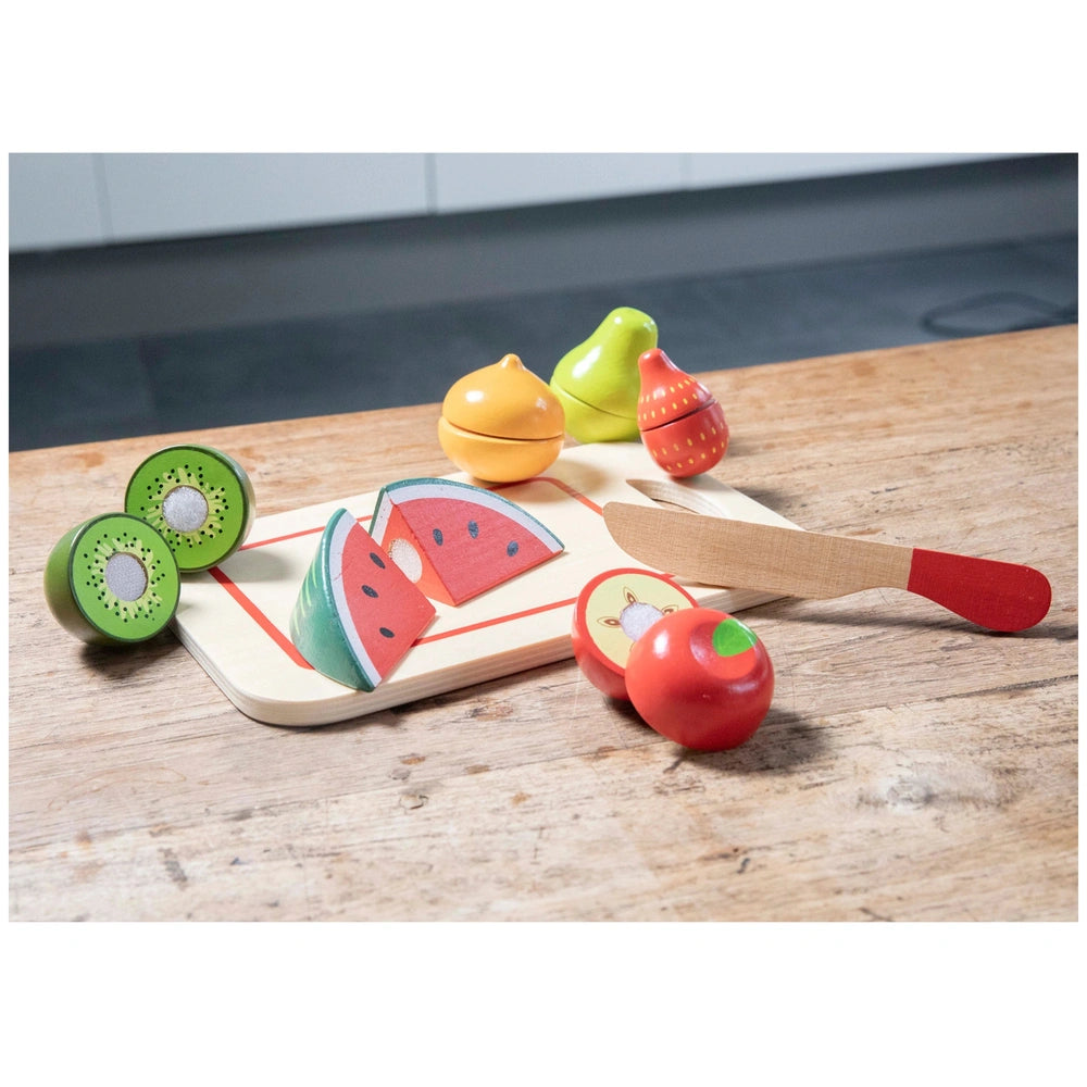 New Classic Toys Cuttingset features plastic fruits: watermelon slices, pomegranate, kiwi, apple, and a red spoon on a wooden