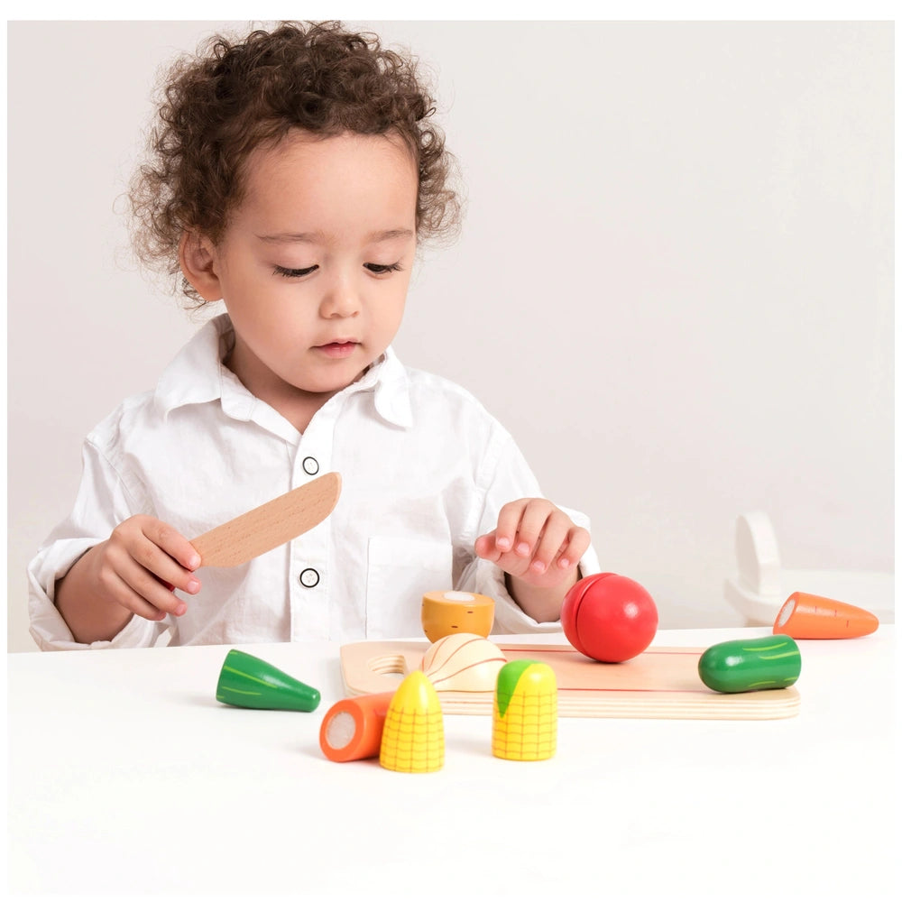 New Classic Toys cutting set features vibrant plastic vegetables like corn, tomato, carrot, and broccoli on a wooden cutting 