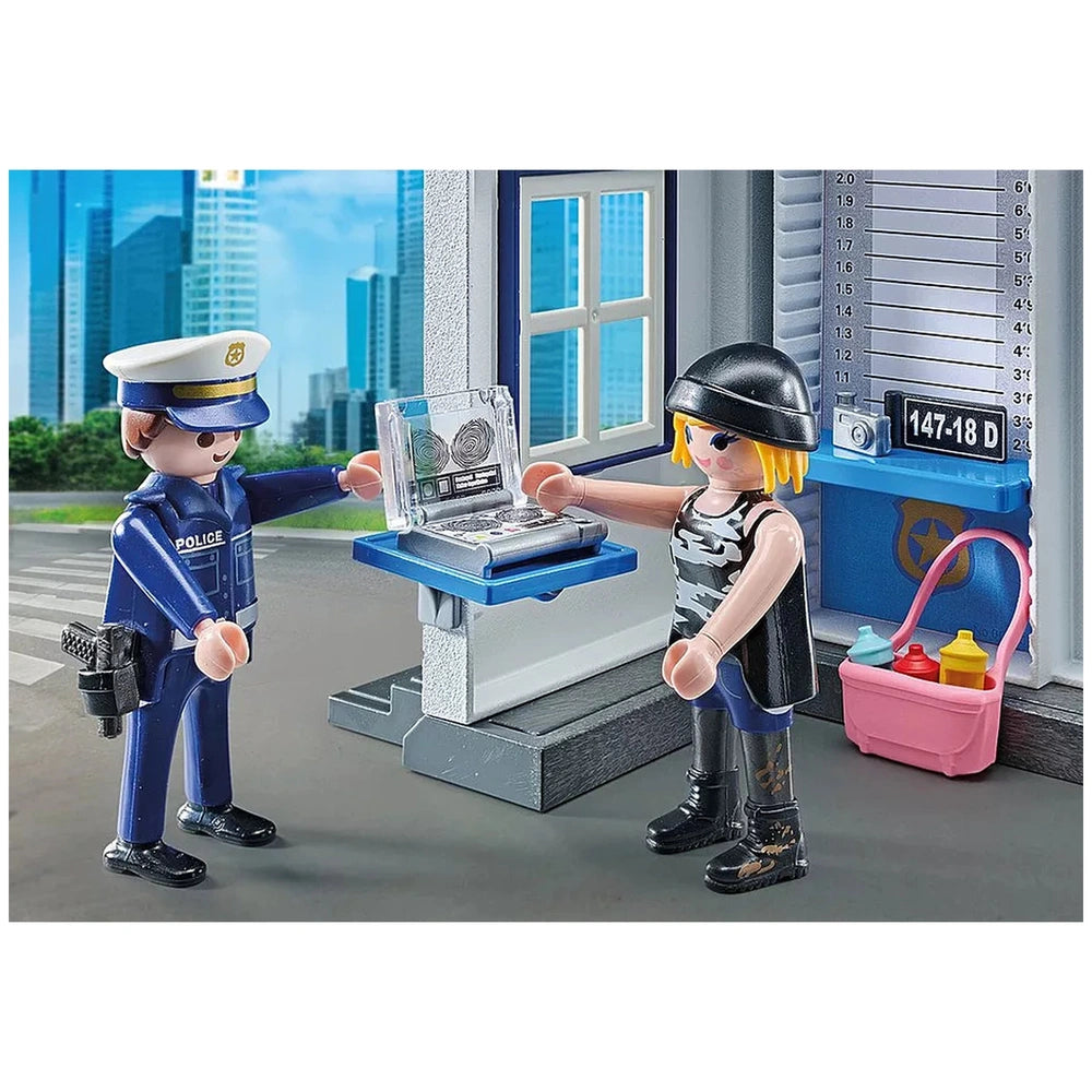 Playmobil Police Interrogation Room features two colorful plastic figures on a gray surface with a blue cityscape background.