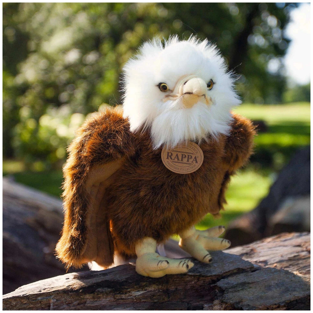 Plush eagle with a white head and brown body perched on a rough wooden surface, featuring a "RAPPA" tag on its chest.