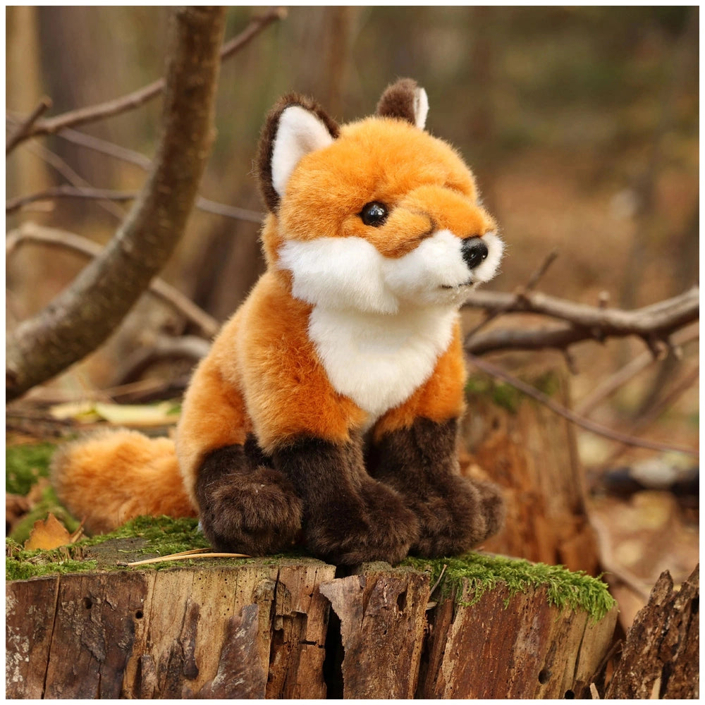 Plush fox stuffed animal with orange and white fur sitting on a tree stump in a blurred woodland background.