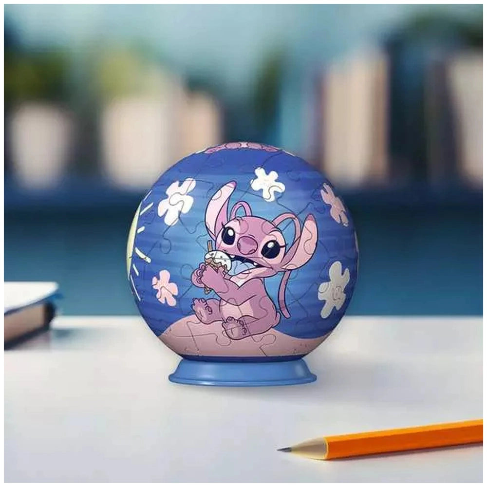 Ravensburger 3D puzzle ball features a blue cartoon character with large eyes, holding a fish against a blurred cityscape bac