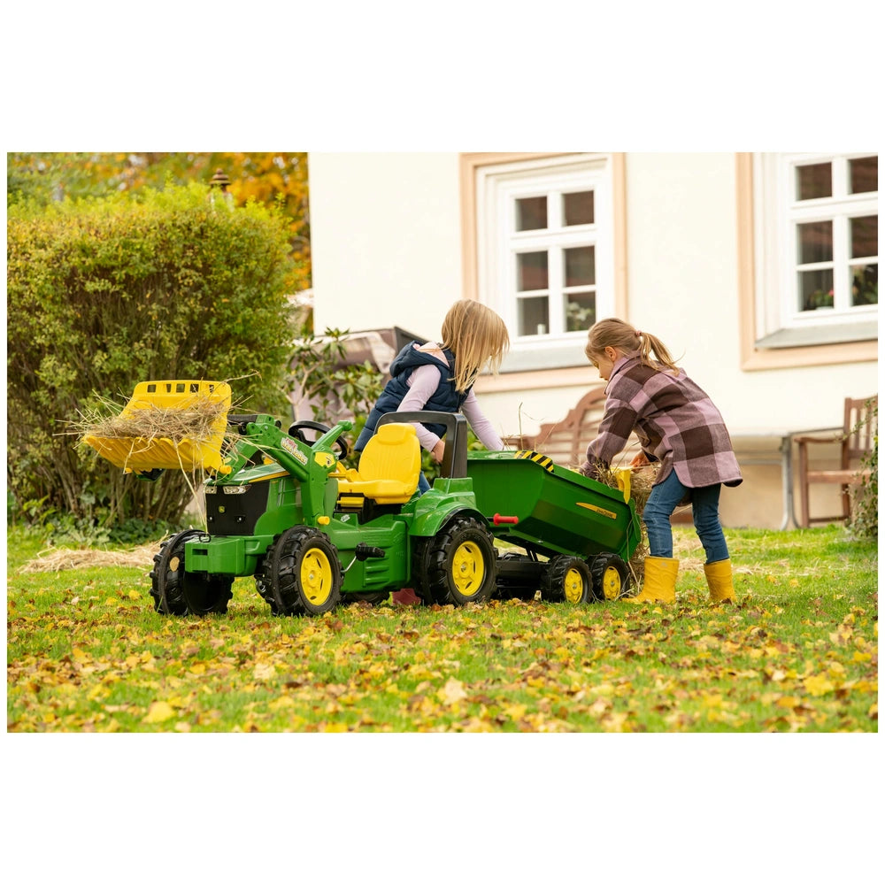 Rollyhalfpipe John Deere trailer toy tractor in green and yellow with girls playing on grass, one examining the scoop filled 
