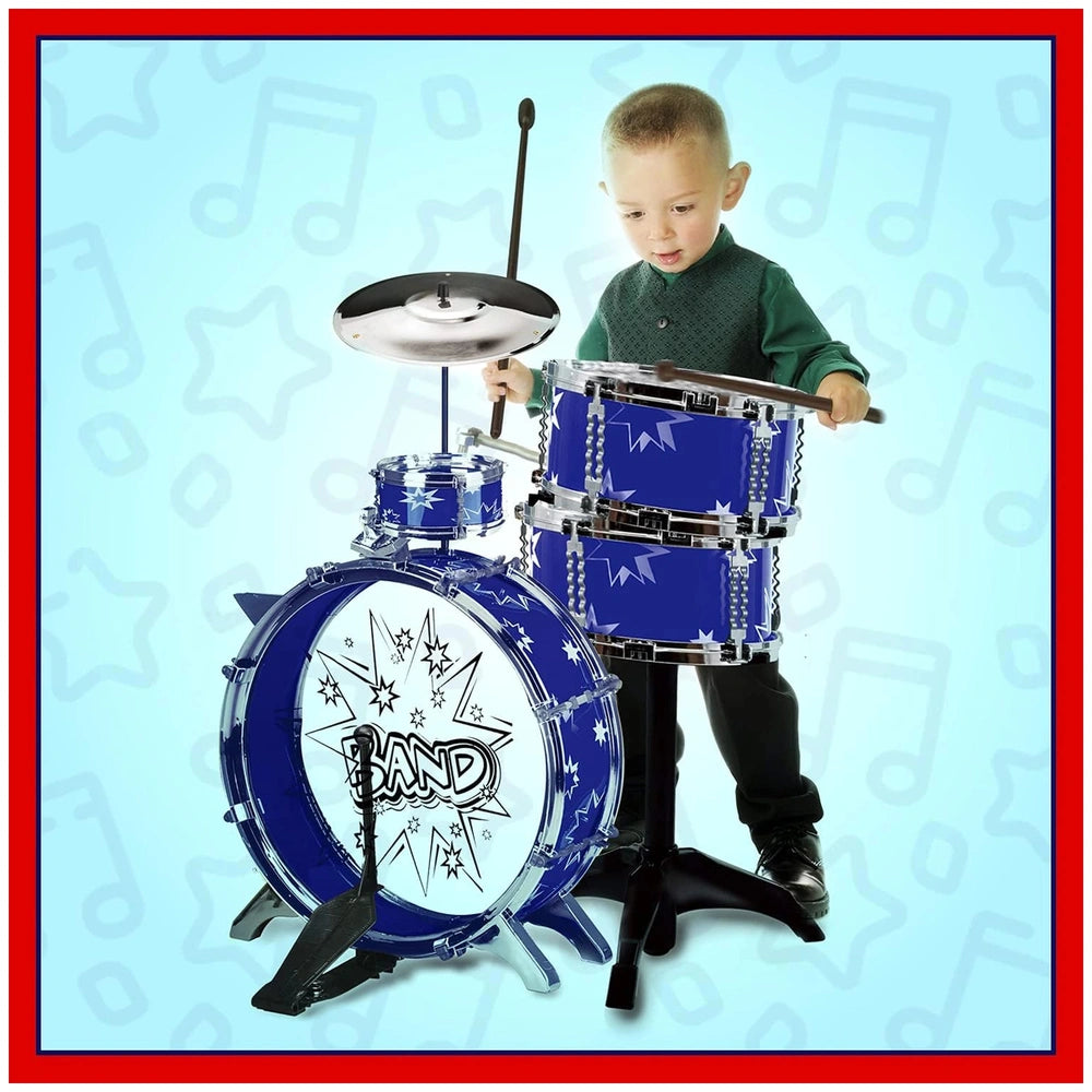 A toddler in a green shirt plays a blue and silver toy drum set with black drumsticks, standing confidently in front.