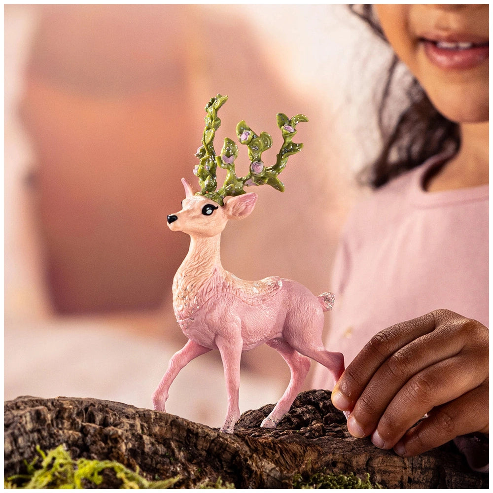 Magic deer figurine in pink hues held by a child's hand, set against a softly blurred warm indoor background.