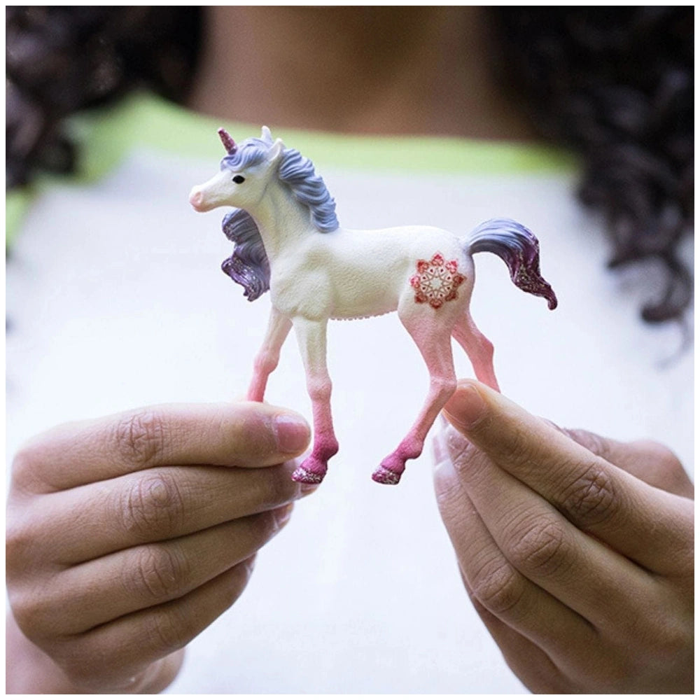 Mandala Unicorn Foal figurine with a white body, blue mane, and pink heart, held in hands against a soft background.