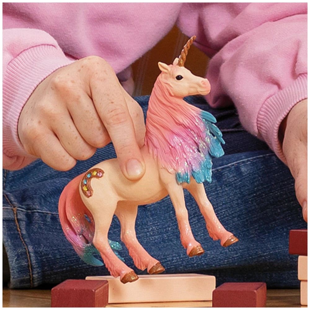 Marshmallow Unicorn figurine with pink mane and tail, standing on a wooden block beside a red block, held by a person.