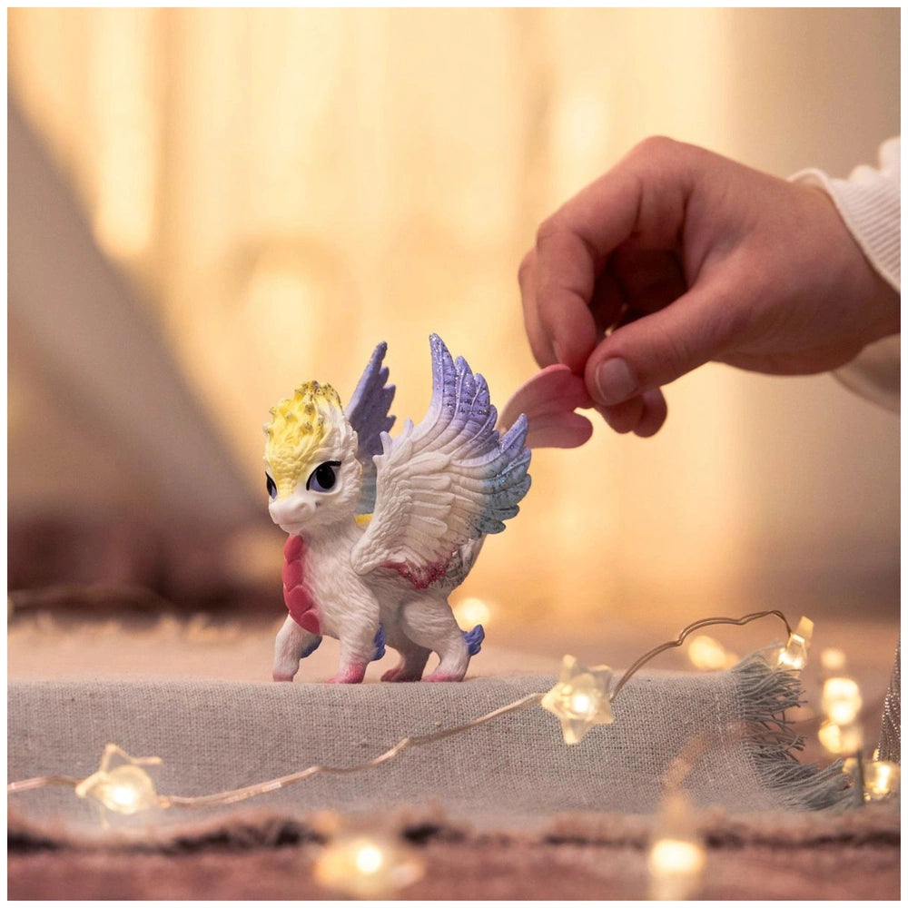 Rainbow Baby Dragon figurine held in a hand, featuring white, blue, and yellow colors against a softly blurred background.