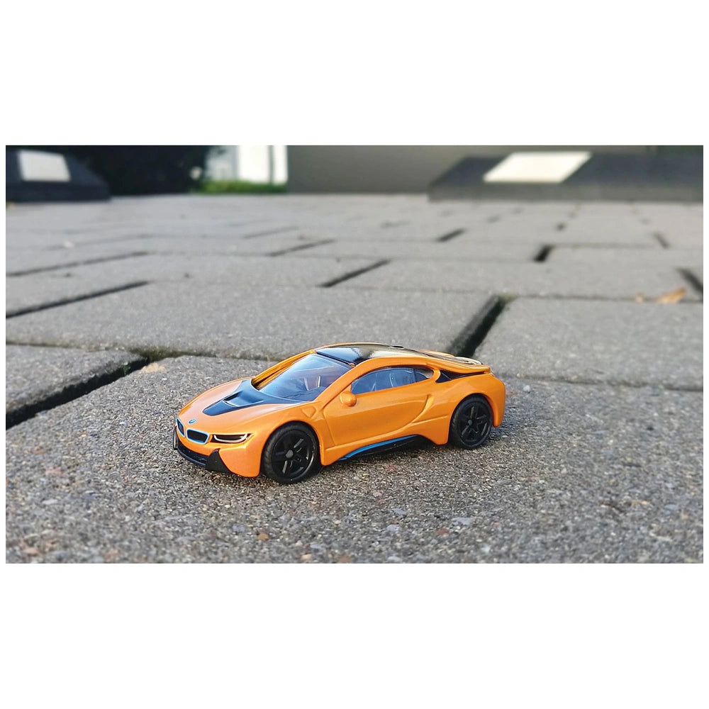 Orange BMW I8 toy car with black accents on a textured concrete surface in an outdoor setting.