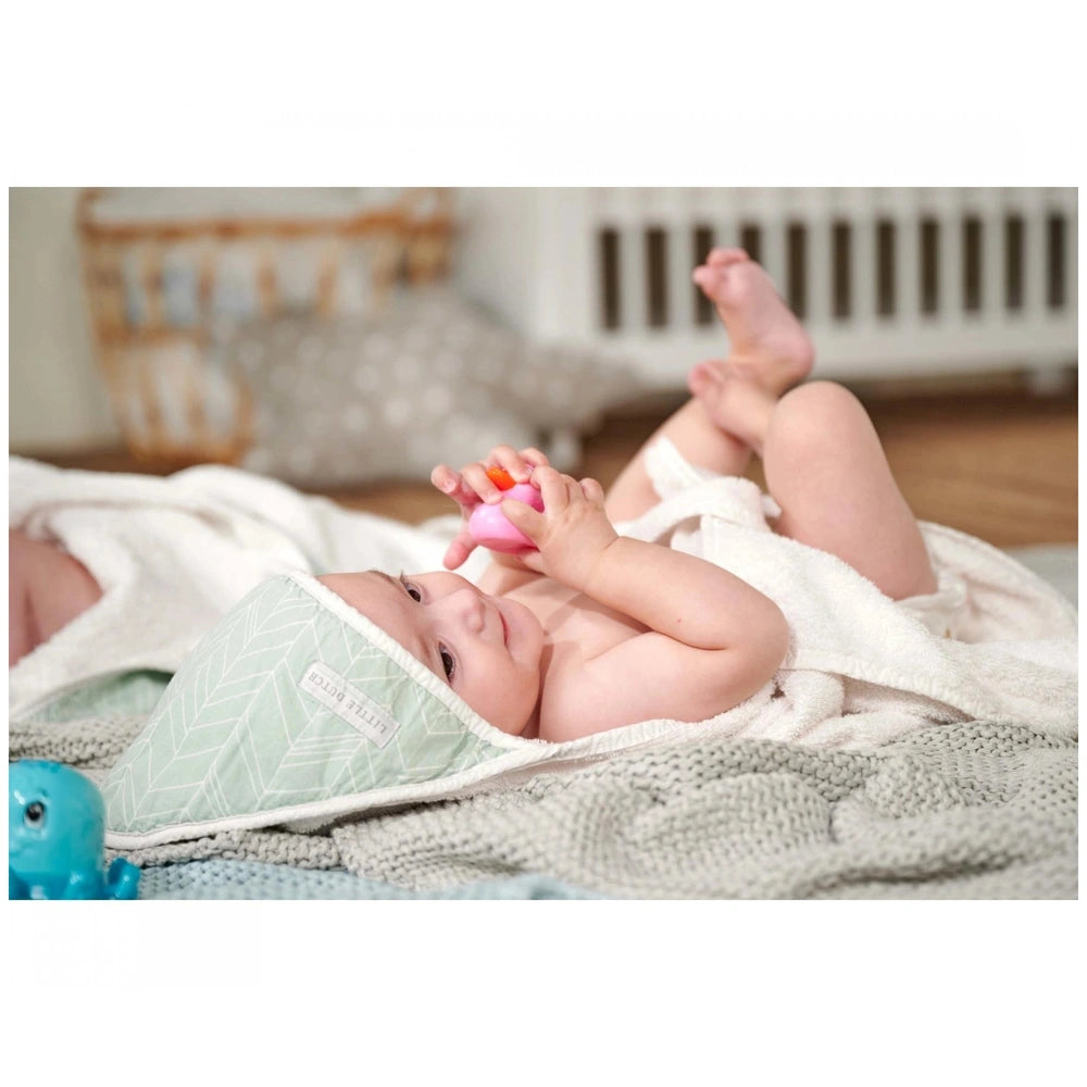 Simba ABC Bathing Ducks - Baby lying on a blanket, wrapped in a towel, holding a toy in a soft pastel nursery setting.