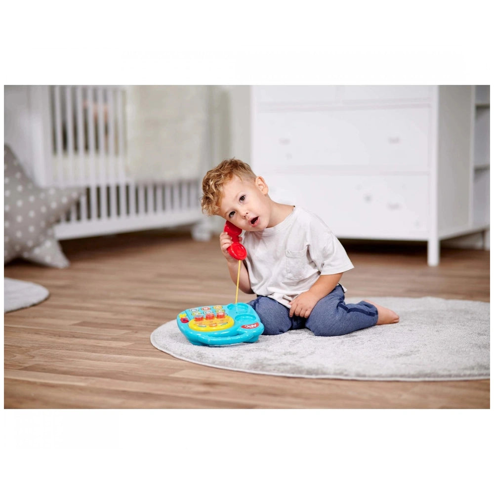 Simba ABC Colorful Telephone - Toddler joyfully using a toy telephone in a bright nursery setting with neutral decor.