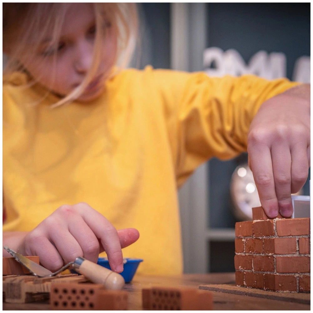 Teifoc garden house set features a child in a yellow shirt building with red Lego bricks on a wooden surface.