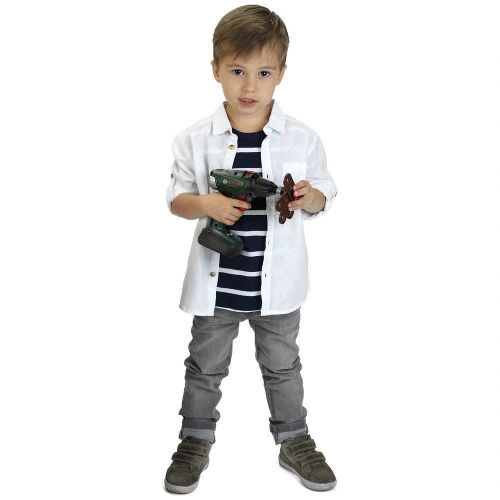 Theo Klein Bosch cordless drill in a child's hands, wearing a white striped shirt and gray pants, holding a screw.