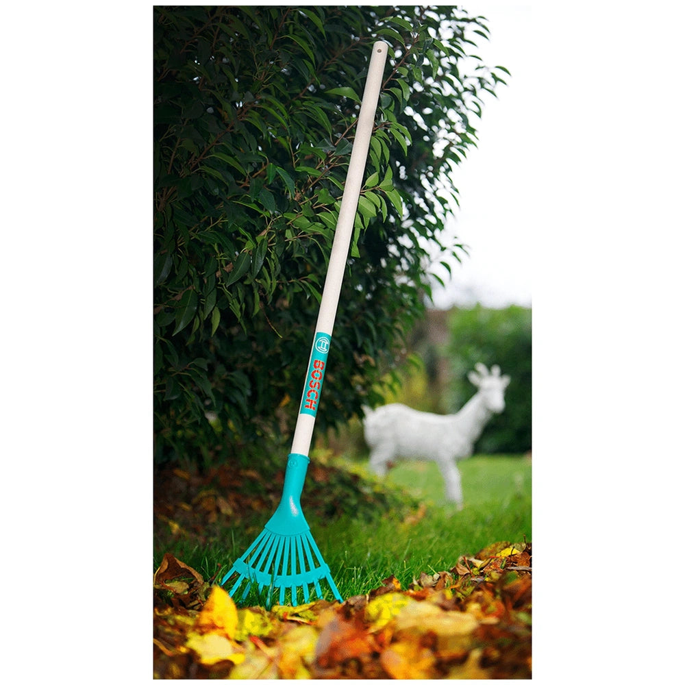 Theo Klein Bosch Garden rake with blue head and white handle, surrounded by yellow and brown leaves on green grass.