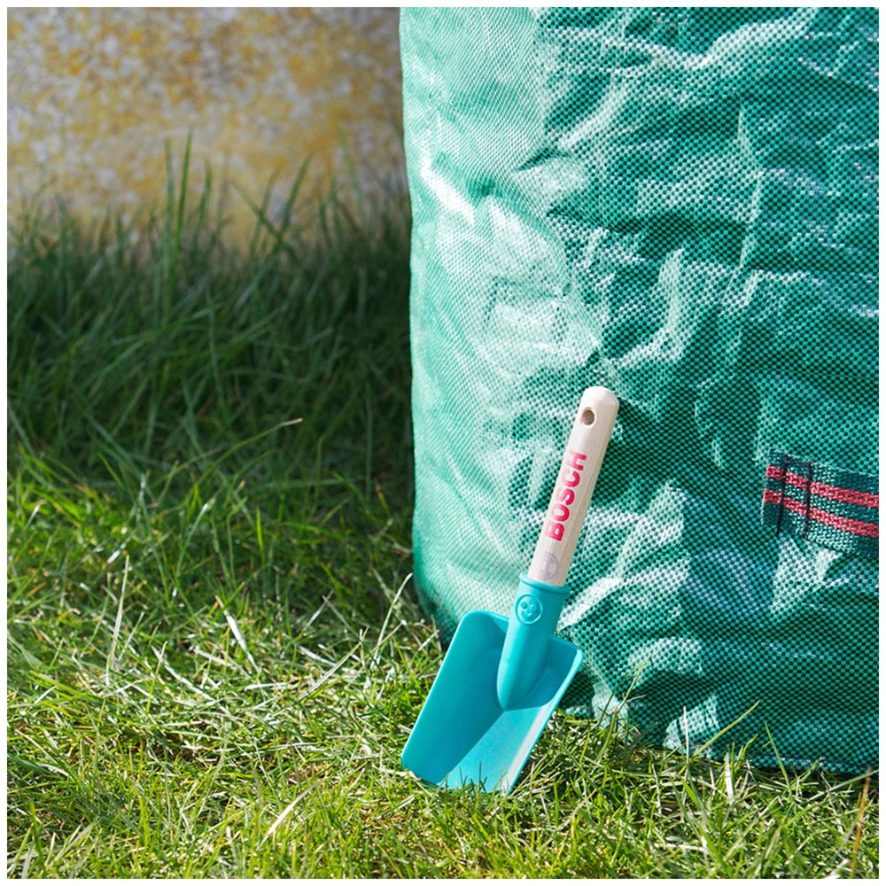 Blue Bosch garden hand shovel with "BUSH" text, placed on green grass next to an indistinct green bag.
