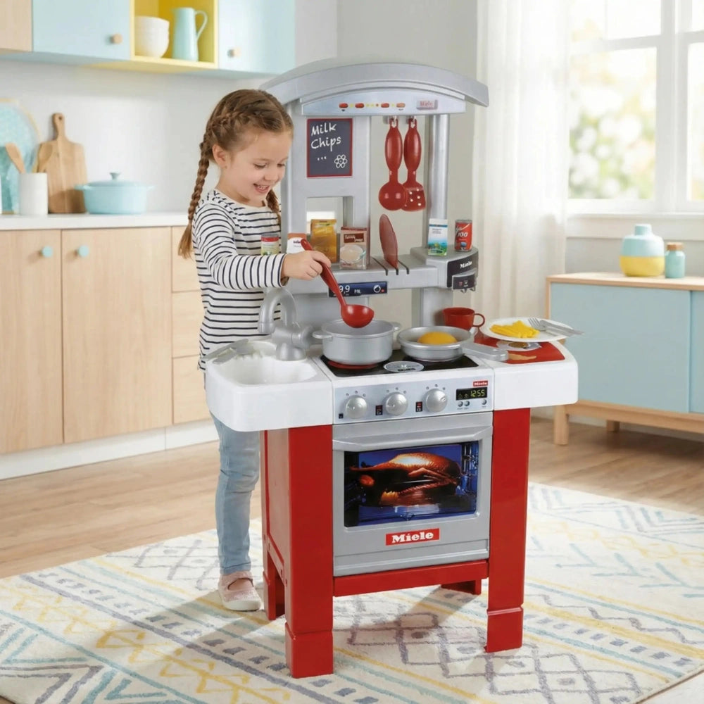 Red and white Theo Klein Miele play kitchen with a child, light wood countertop, and blue wall in a vibrant playroom scene.